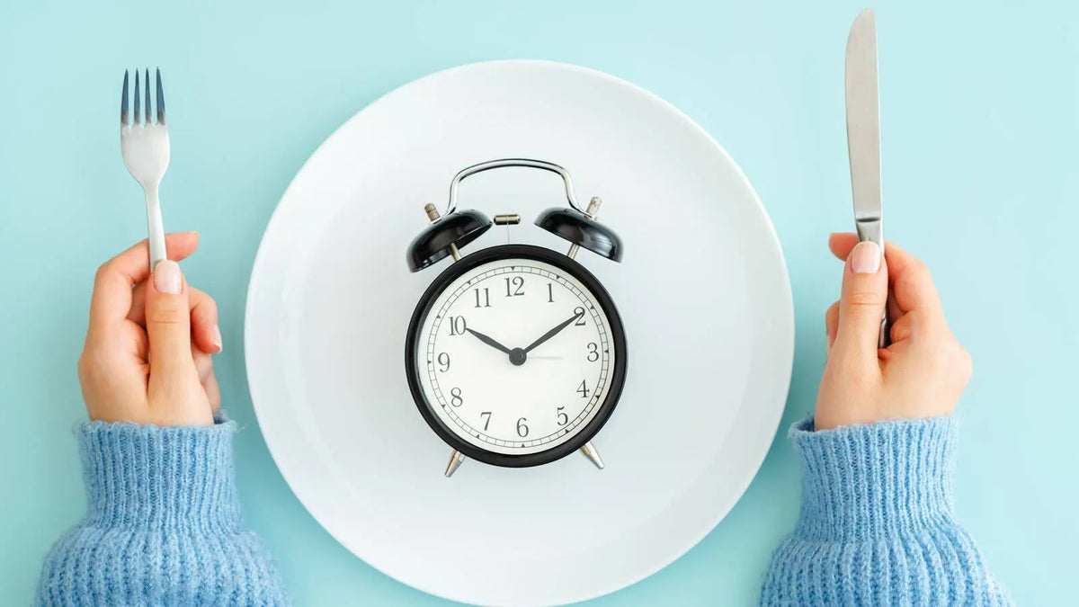 clock on dinner plate with person holding fork and knife