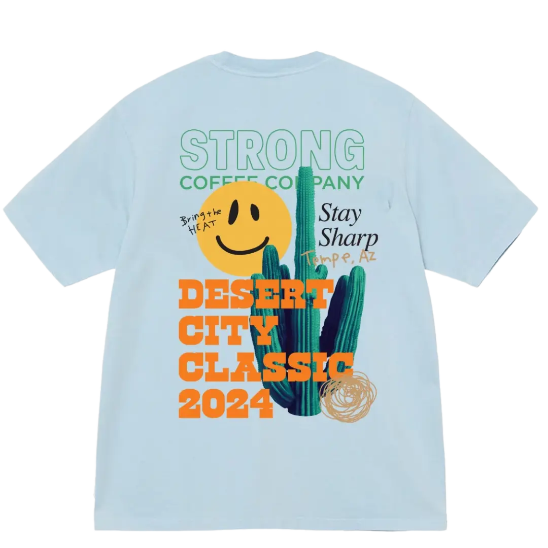 A light blue t-shirt with text and graphics related to the Desert City Classic competition, including a smiley face and cactus design.